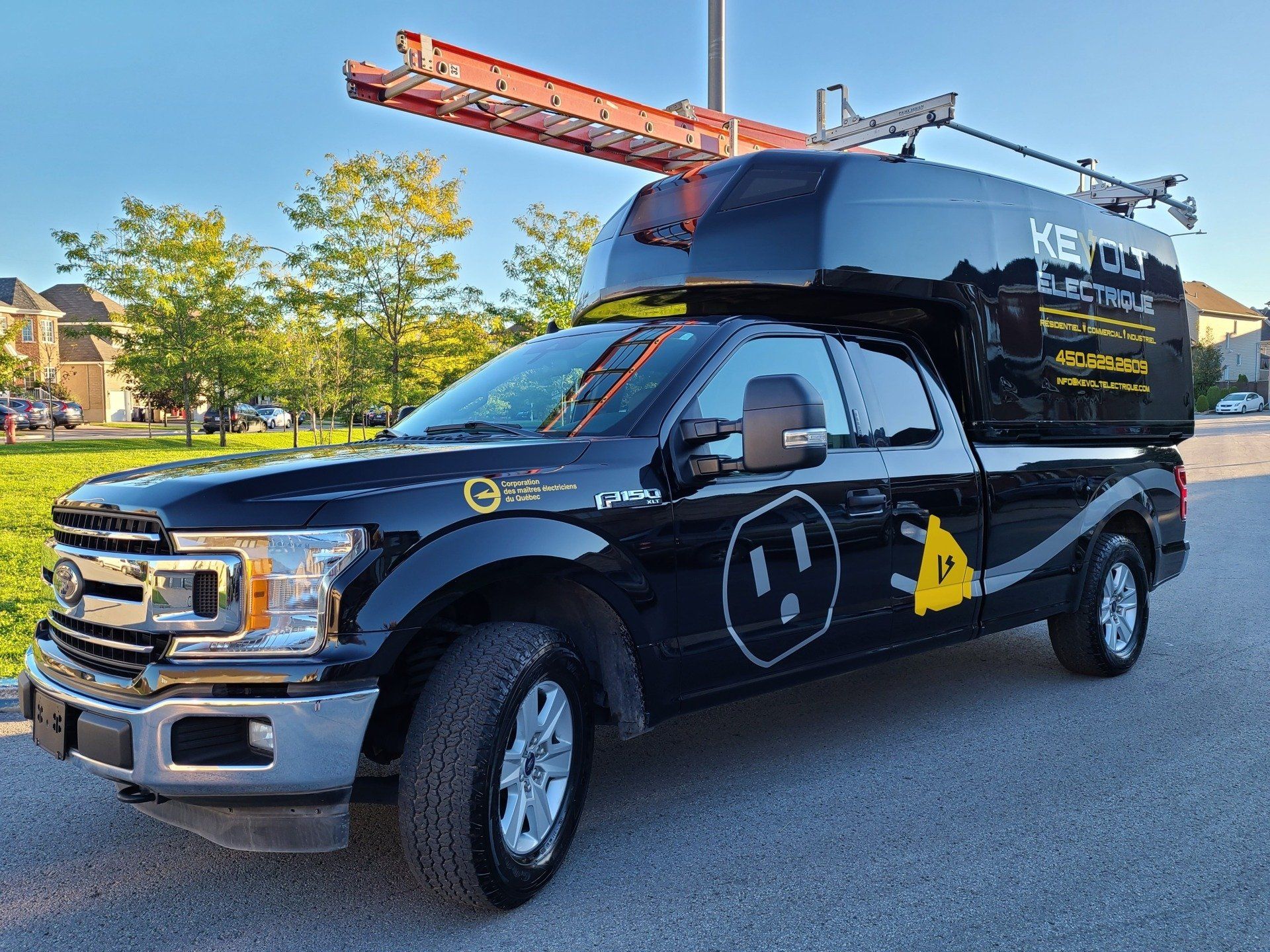A black truck with a ladder on top of it is parked on the side of the road.