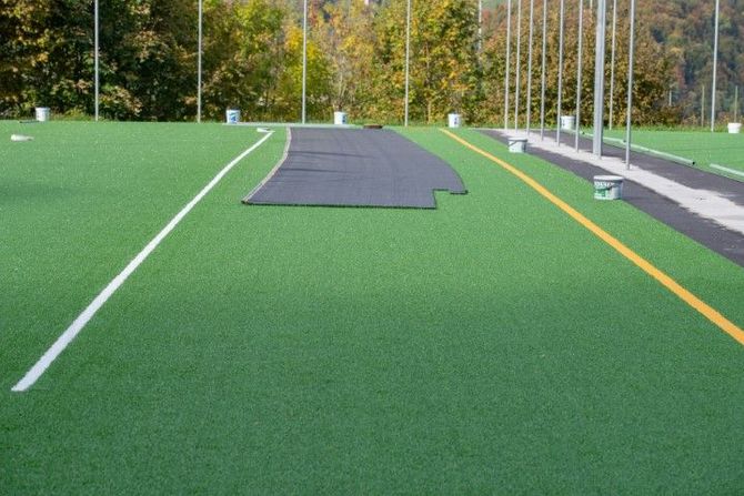 Artificial turf field under construction with a large black mat and markings on the green surface.