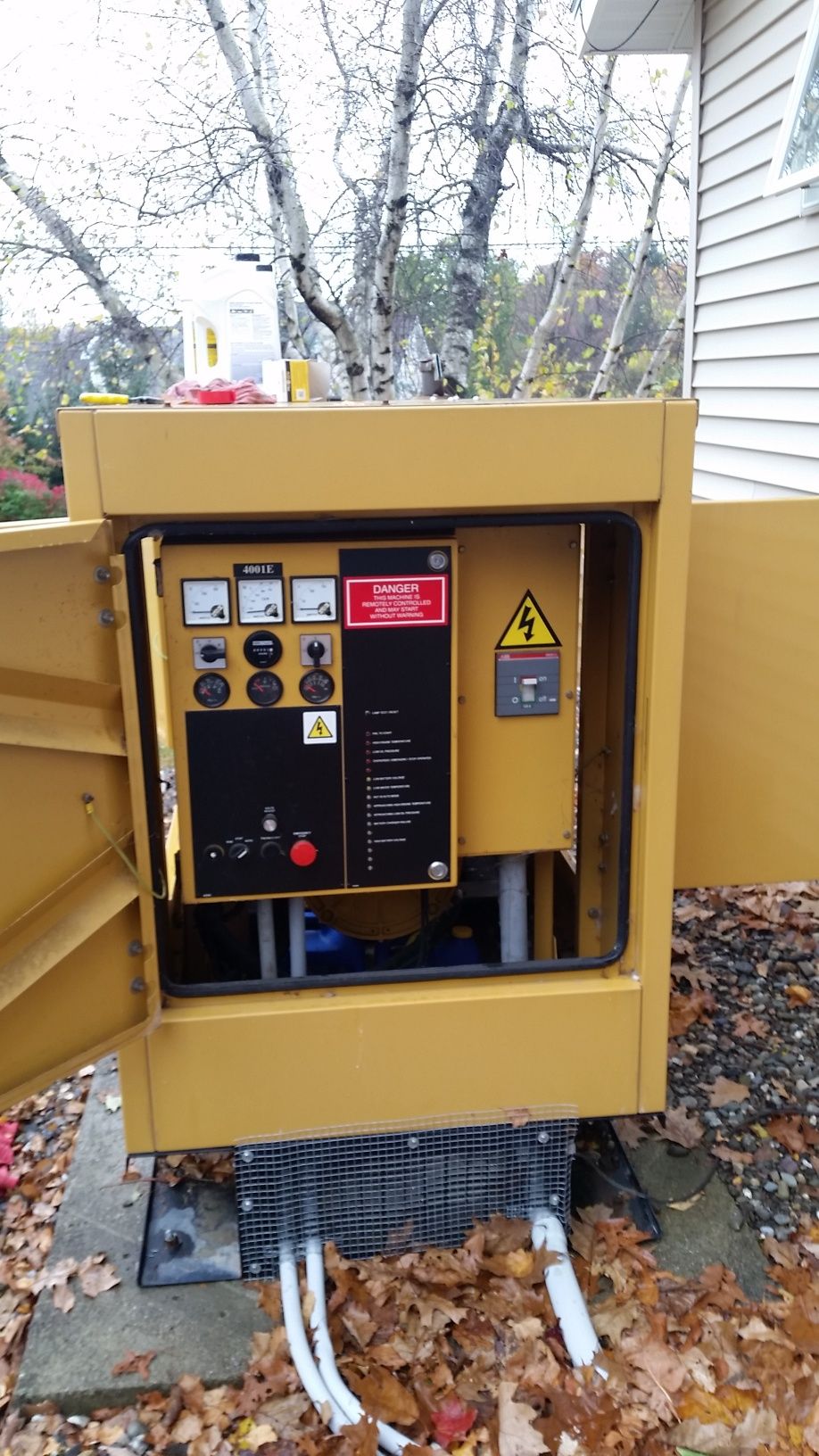 Yellow industrial machine with control panel and warning signs outdoors beside a house
