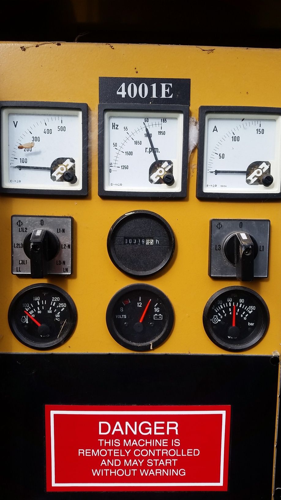 Yellow industrial control panel with gauges, switches, and a red danger warning label.