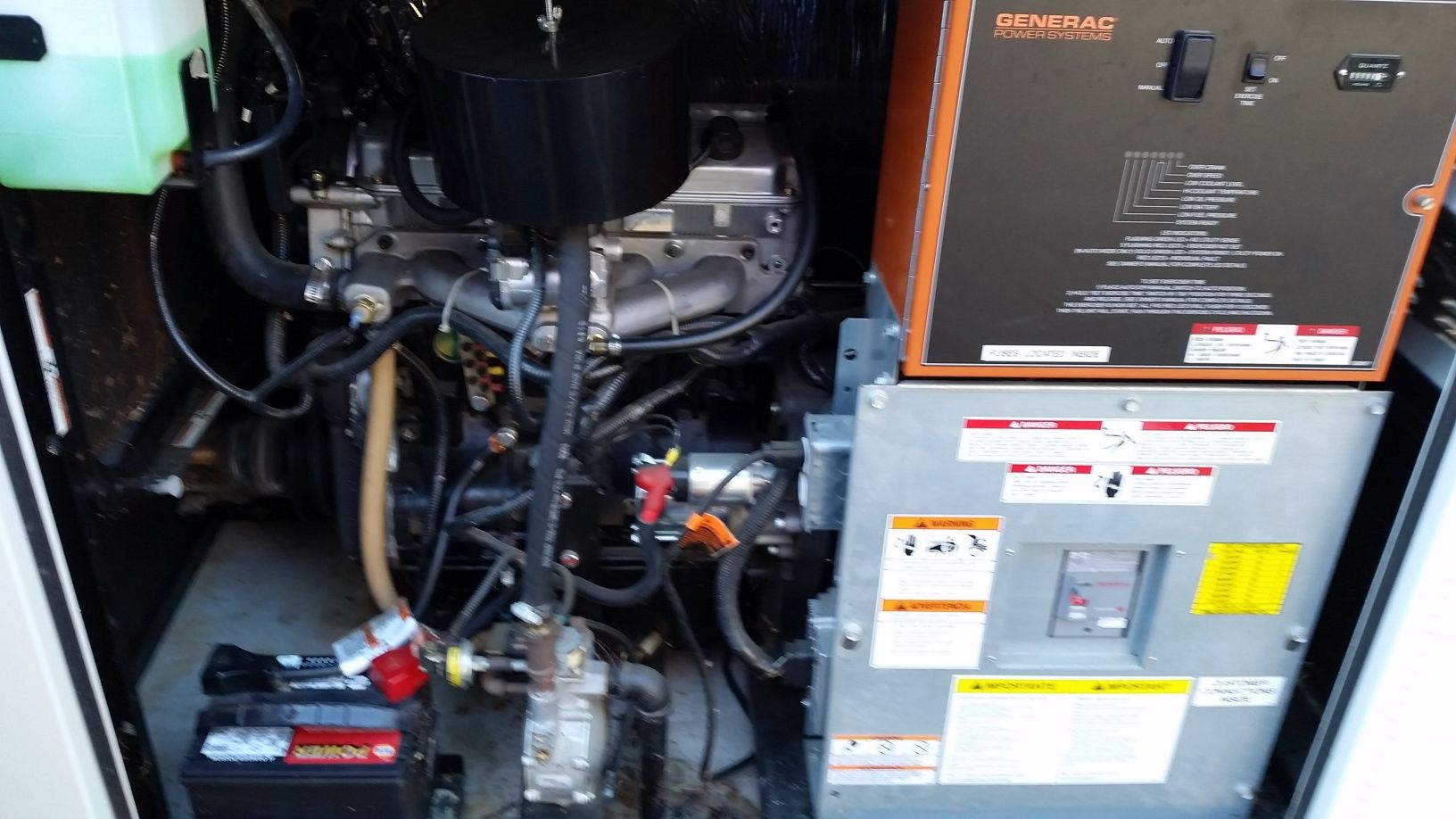 Open generator compartment with black engine, hoses, and gray electrical panels inside a cabinet