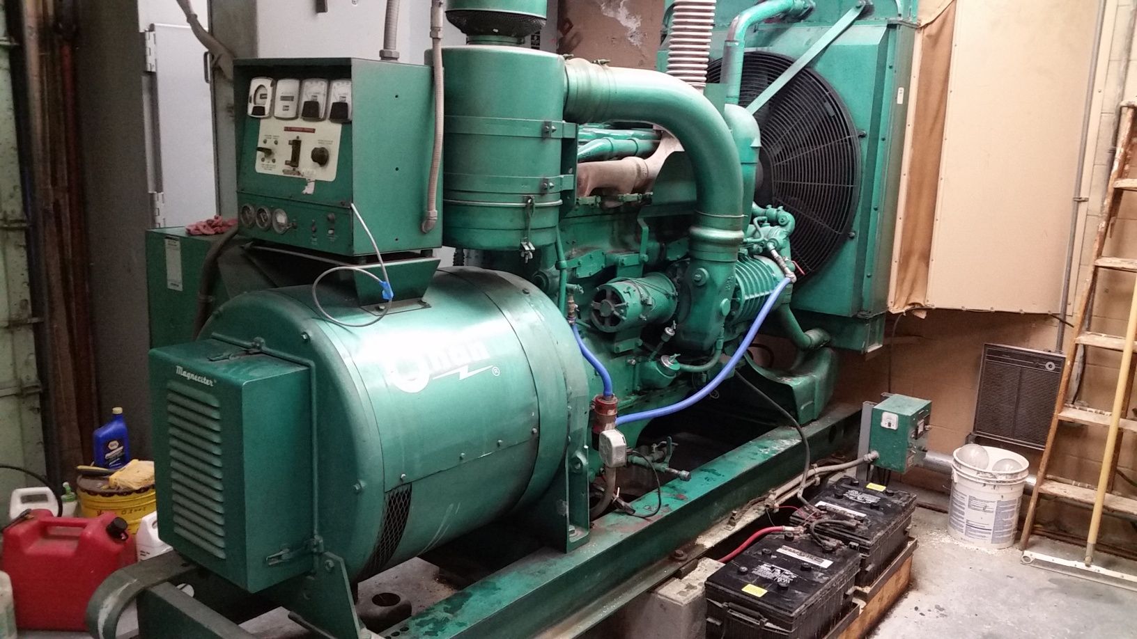 Large green industrial generator in a utility room with pipes, gauges, and control panels