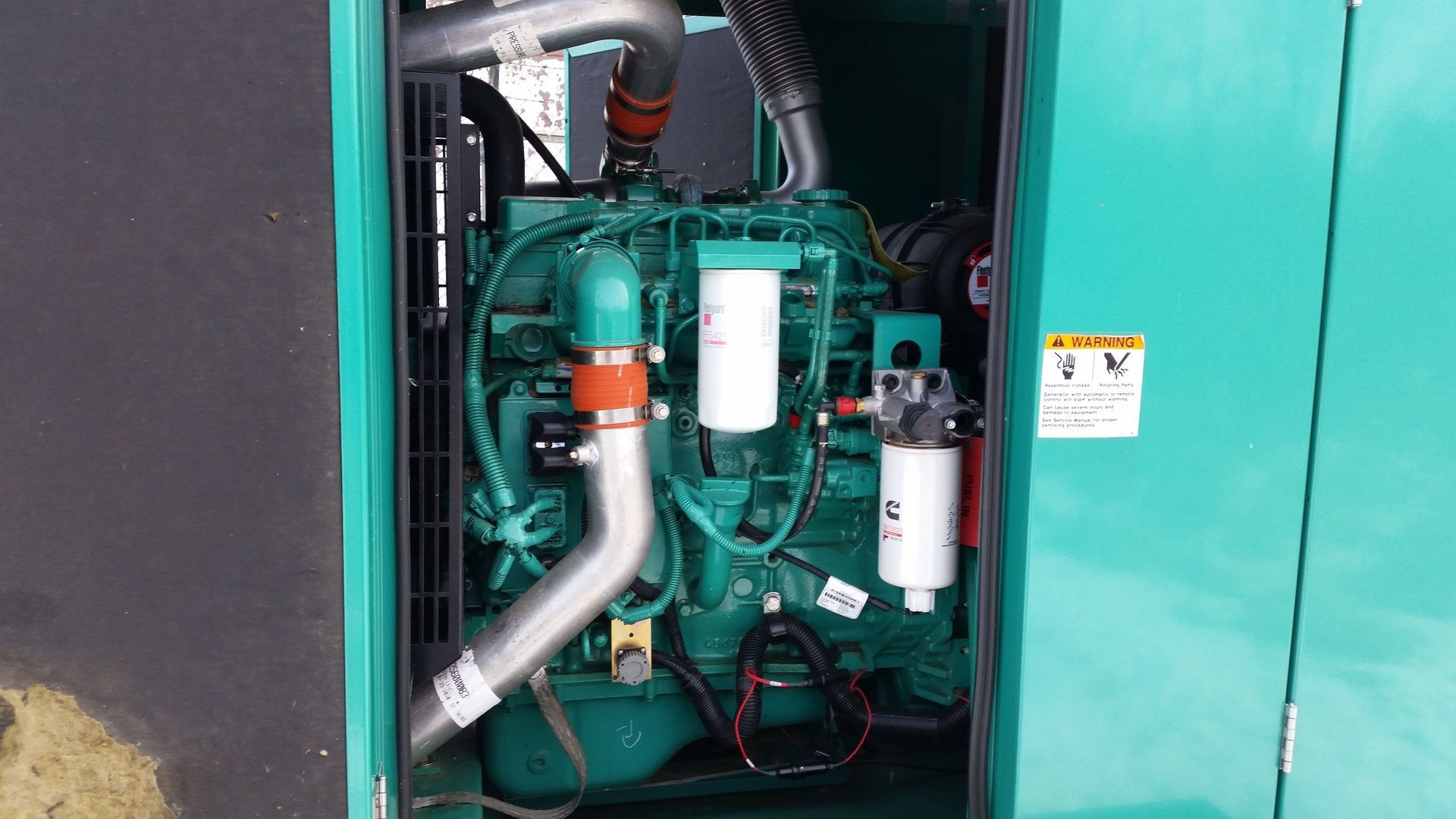 Green industrial generator with exposed engine and pipes inside an open cabinet