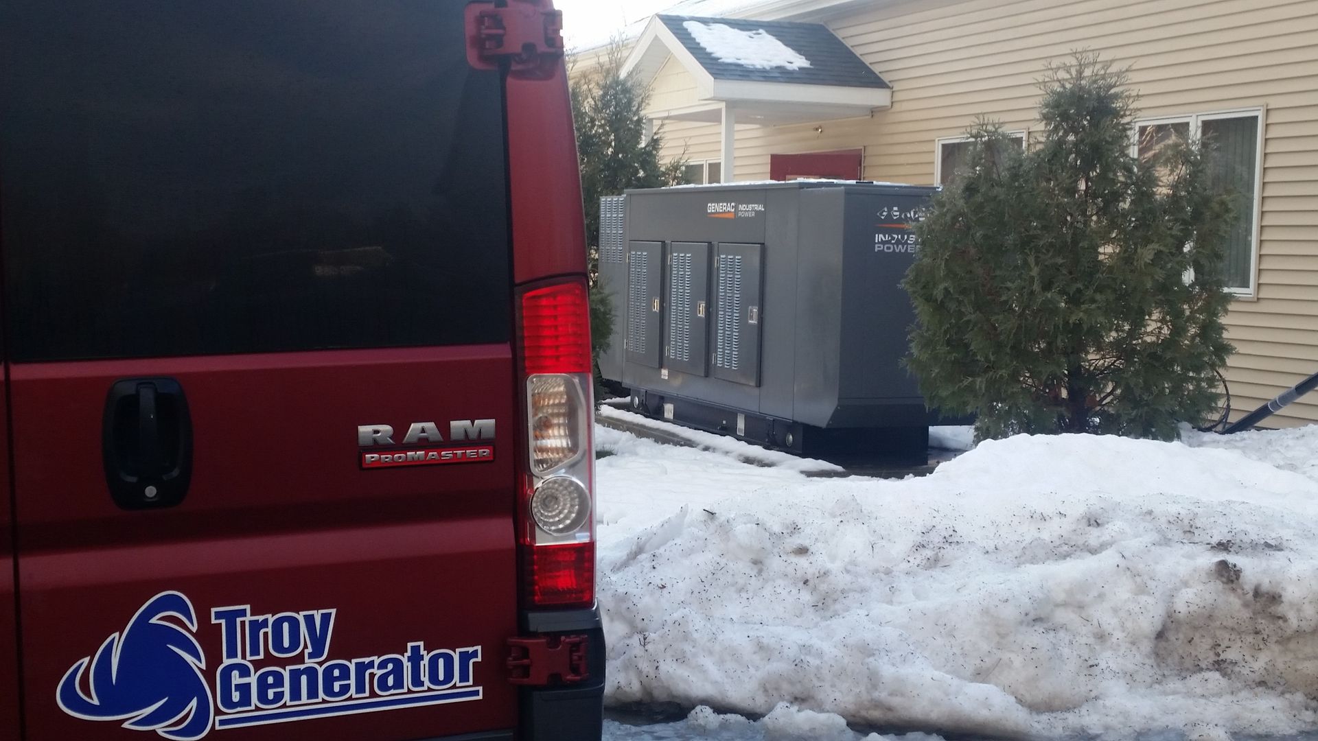 Red Troy Generator van beside snow-covered HVAC units outside a building