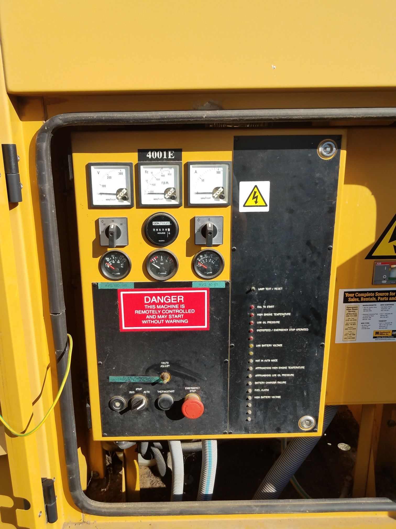 Yellow industrial control panel with gauges, switches, warning labels, and a red emergency stop button