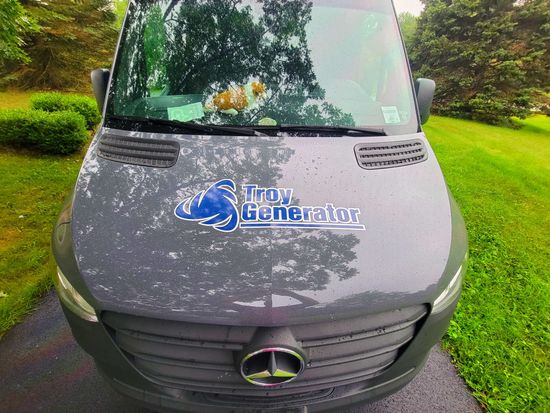 Gray van with “Show Generator” logo on hood, parked on grass outdoors.