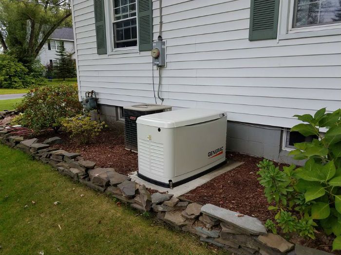 Whole-house generator beside a white house, set on a gravel pad near the foundation.