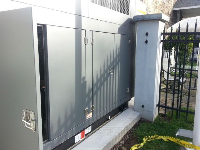 Gray metal gate and fence beside a narrow walkway, with a white wall and black railing in the background.