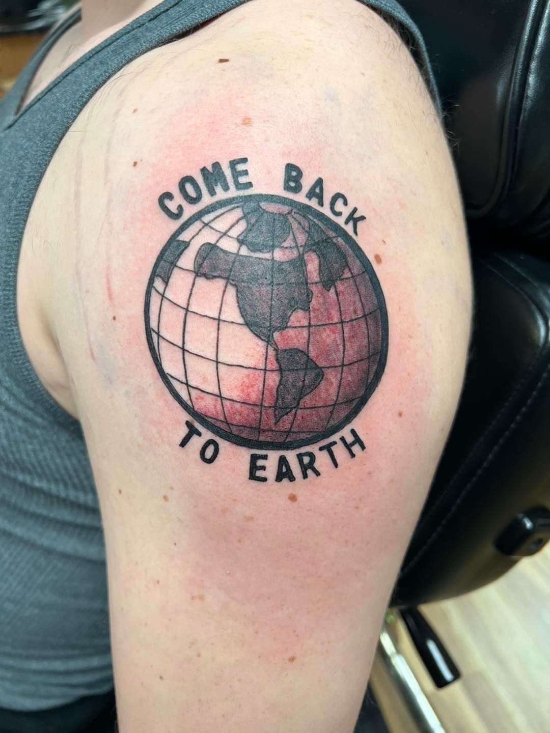Shoulder tattoo of a pink globe with the words “COME BACK TO EARTH” around it