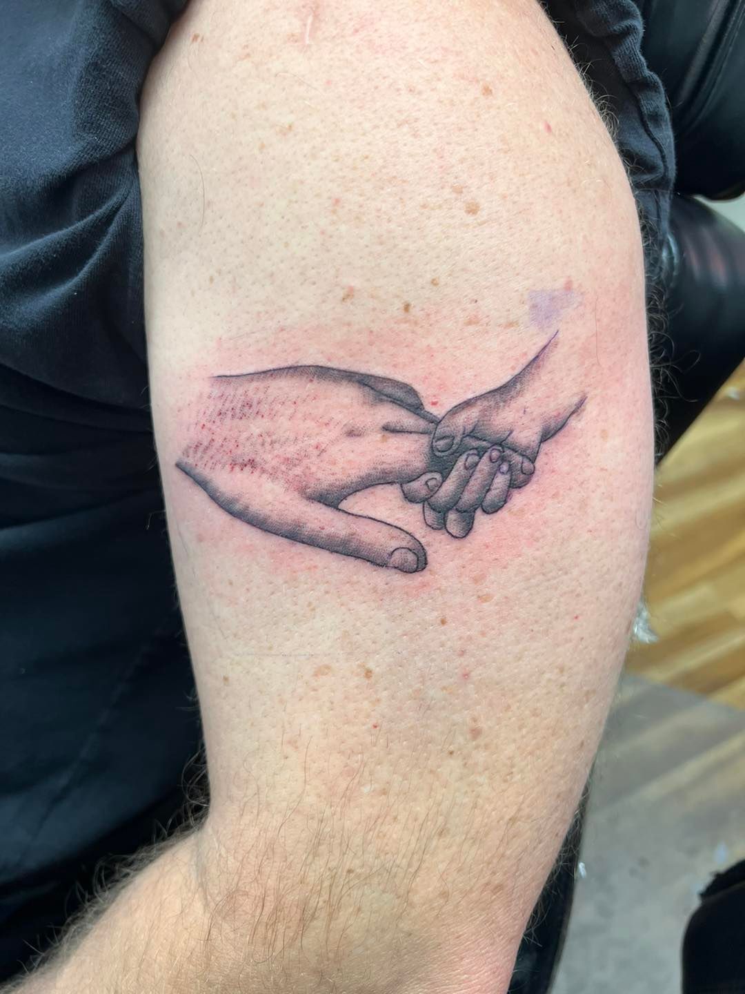 Black ink tattoo of two hands touching on a person’s upper arm