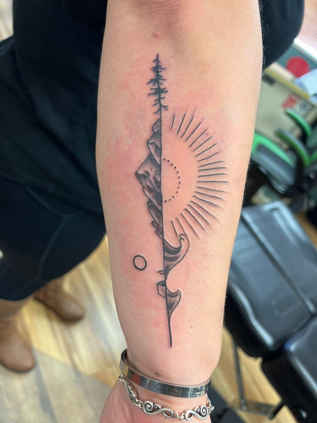 Forearm with a black vertical tattoo featuring a sunburst and crescent moon design
