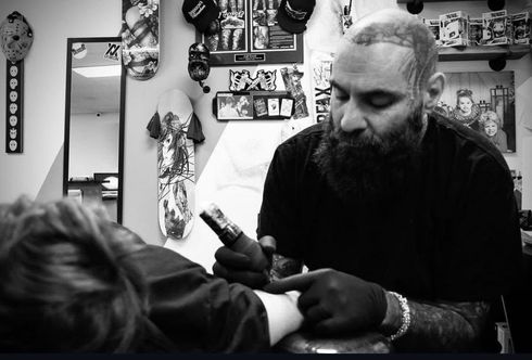 Tattoo artist using a machine on a client in a studio, black-and-white scene