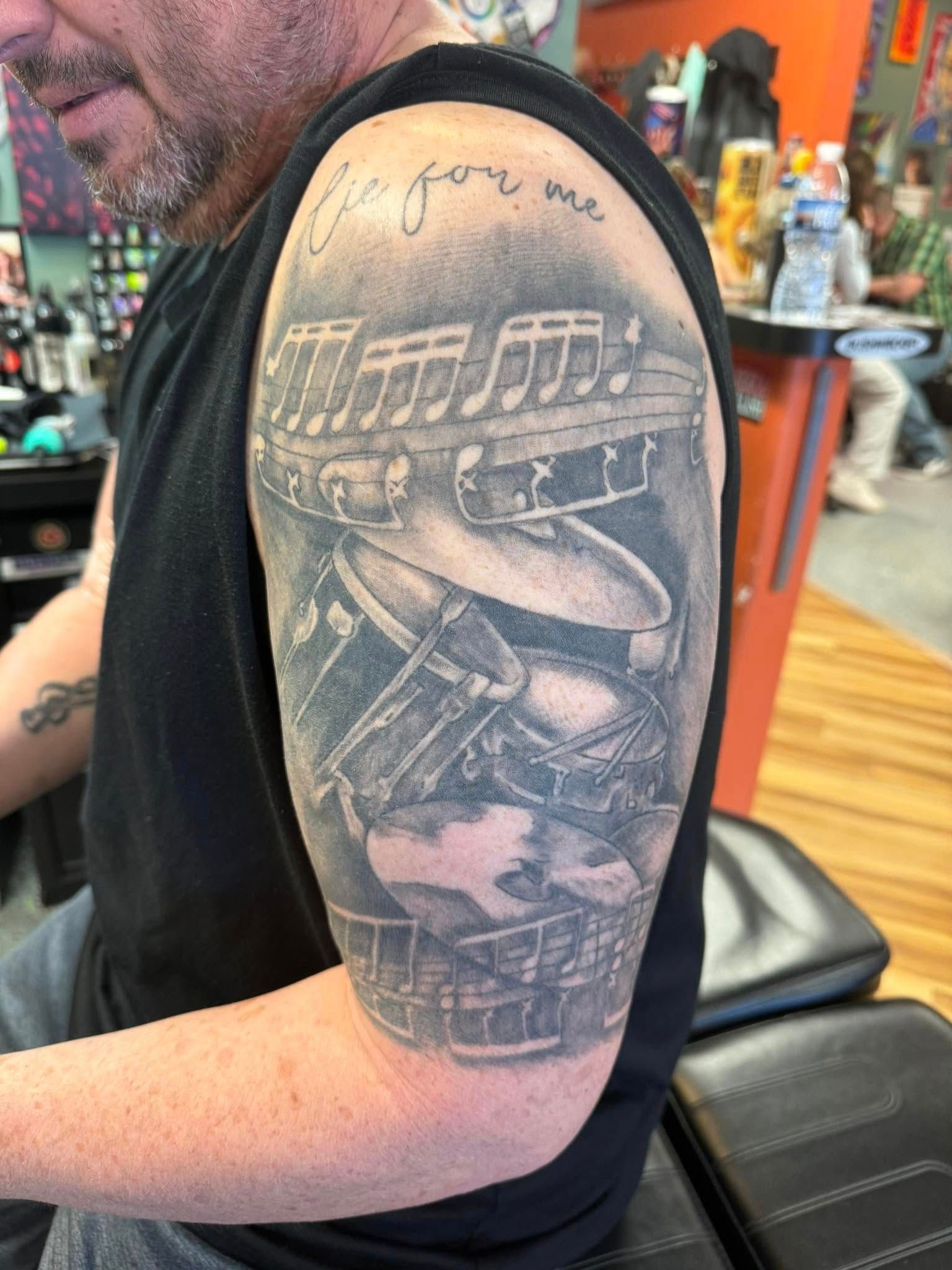 Close-up of an upper arm tattoo in black and gray, showing a sneaker with layered geometric details.