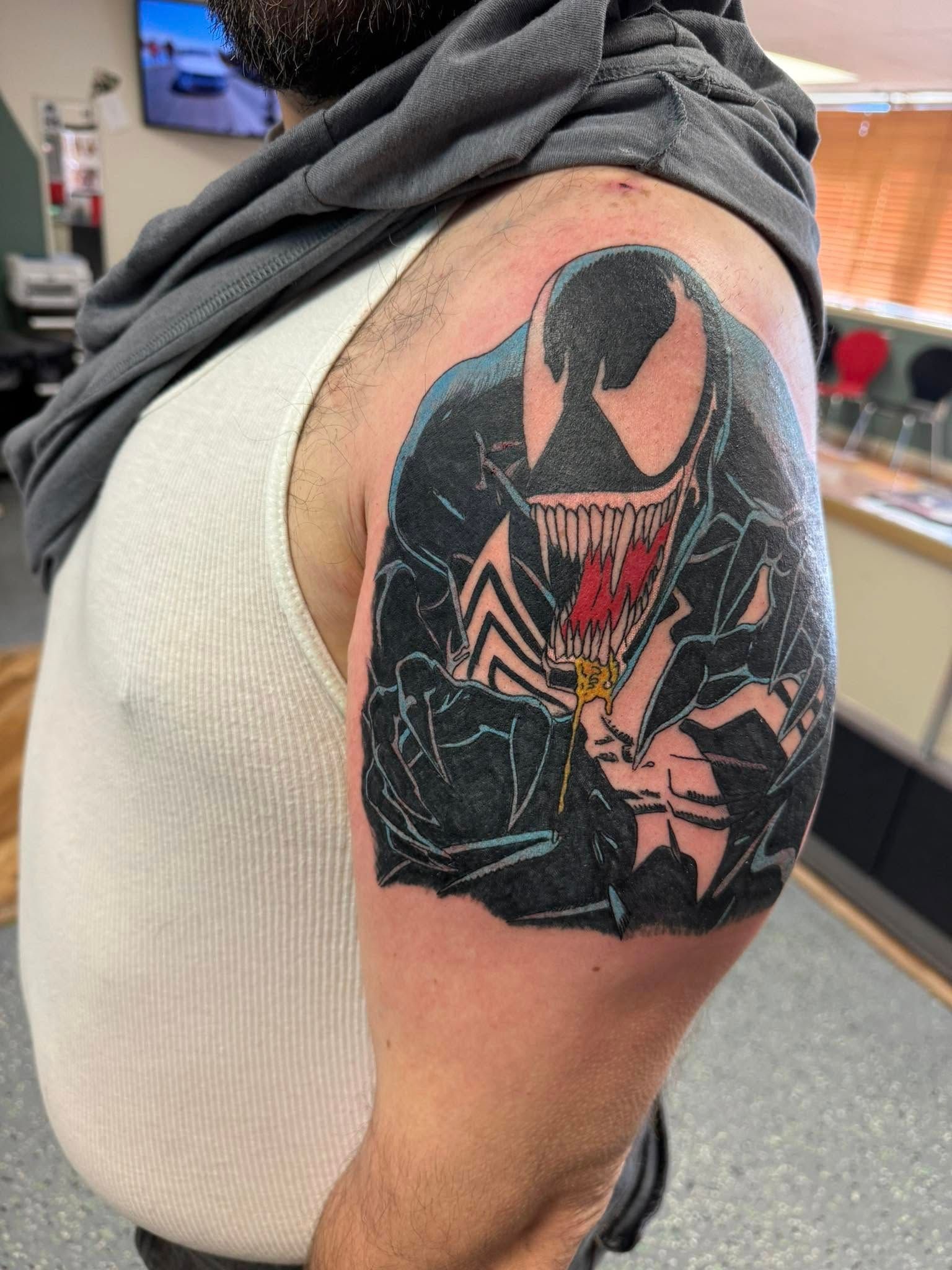 Upper arm with a colorful Venom tattoo on a person wearing a white tank top.