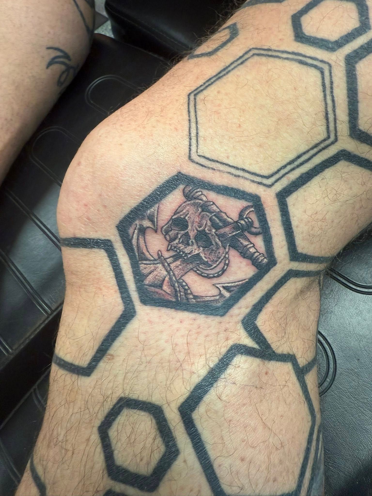 Black-and-gray hexagon tattoos on a person’s leg, with a central floral design.