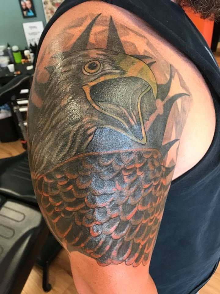 Close-up of a black-and-orange crow tattoo on a person's upper arm in a tattoo shop