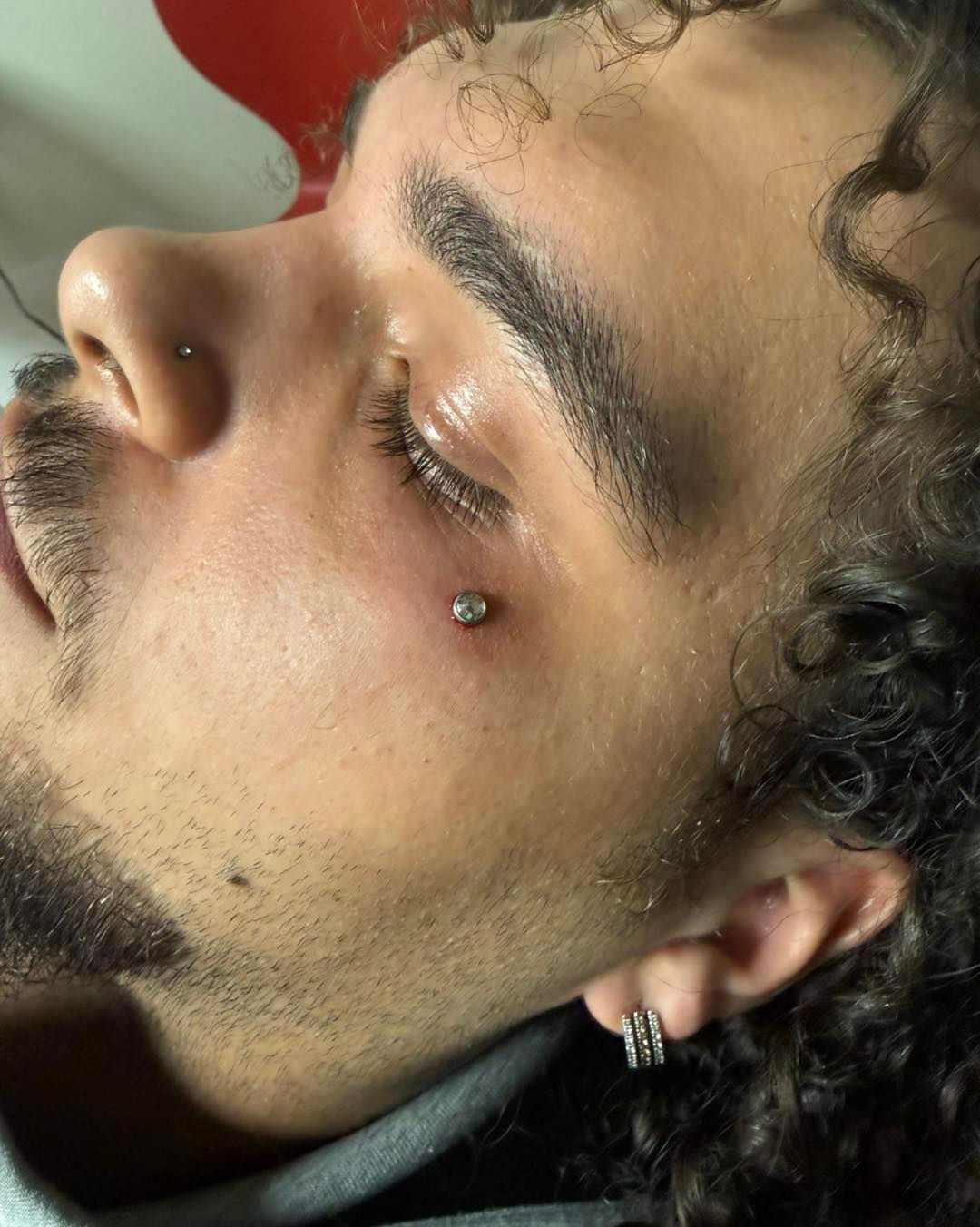 Close-up profile of a person with curly hair and a nose piercing, wearing an earring and looking downward.