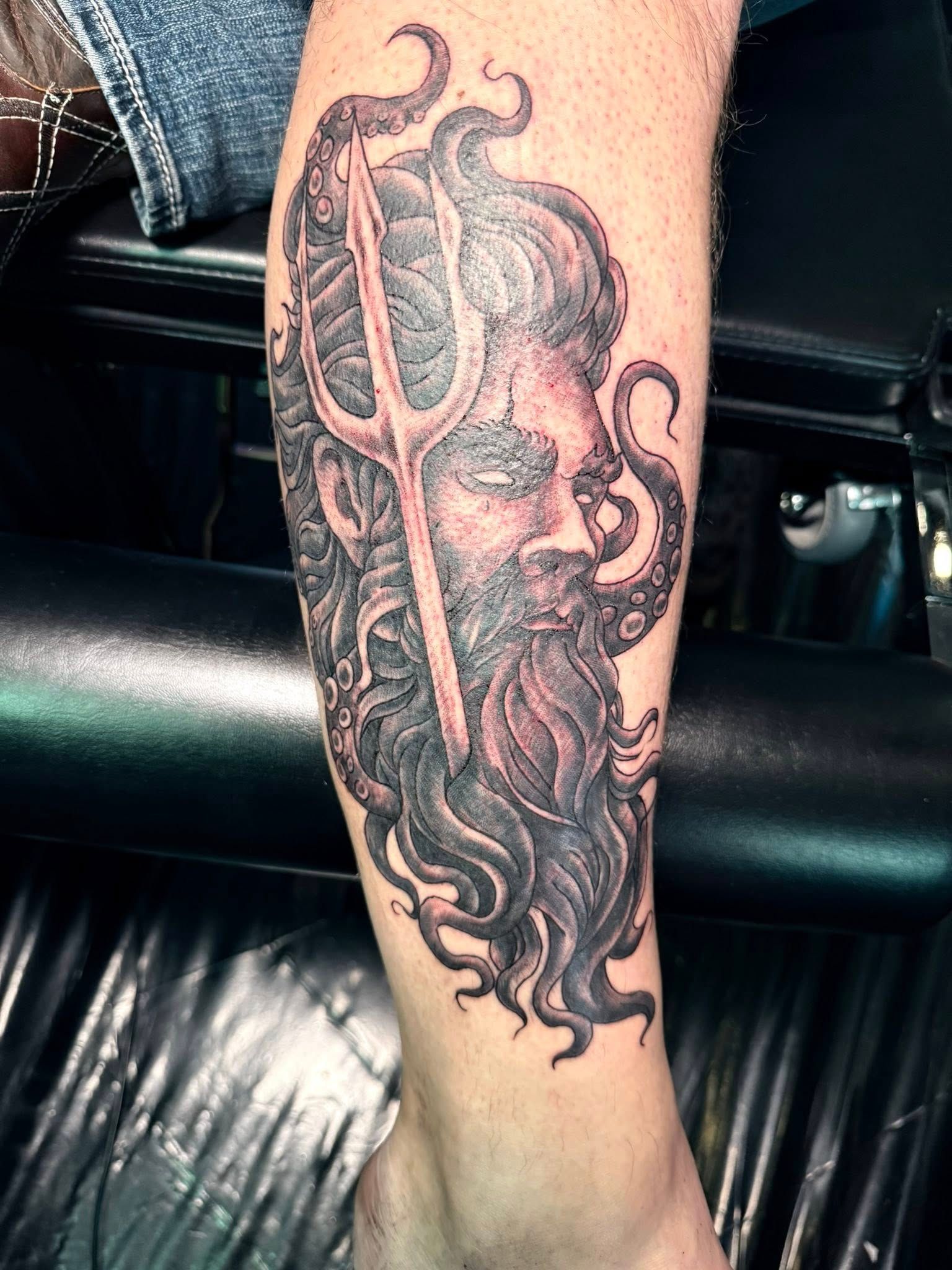 Detailed black-and-red tattoo of a bearded face with swirling hair on a person's forearm