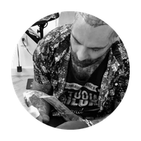 Person with beard looking down while working on a tattoo or drawing in a studio
