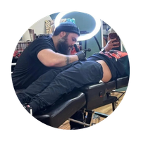 Tattoo artist working on a client’s leg under a ring light in a studio