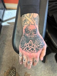 Person’s back with a large black-and-gray skull and bat tattoo, viewed indoors.