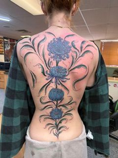 Person’s upper back with a large floral tattoo design in black and pink.