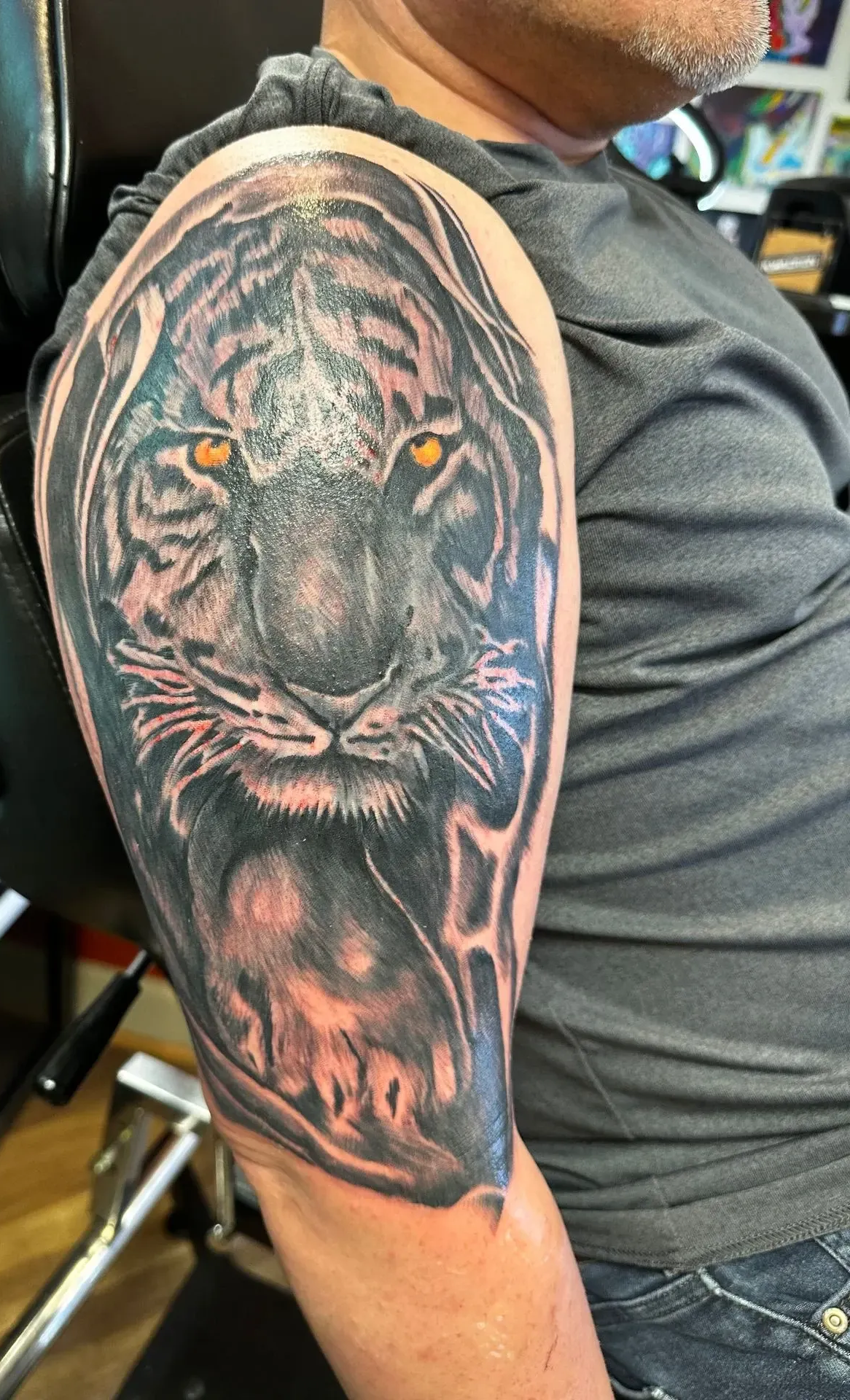 Upper arm tattoo of a black panther portrait on a seated person, with pink-orange highlights.