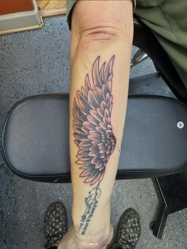 Forearm with a black vertical tattoo featuring a sunburst and crescent moon design
