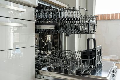 An open, empty dishwasher with two pull-out wire racks and a black utensil basket in a modern, white kitchen.
