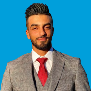Man in a gray suit with a red tie, standing against a bright blue background, facing the camera.