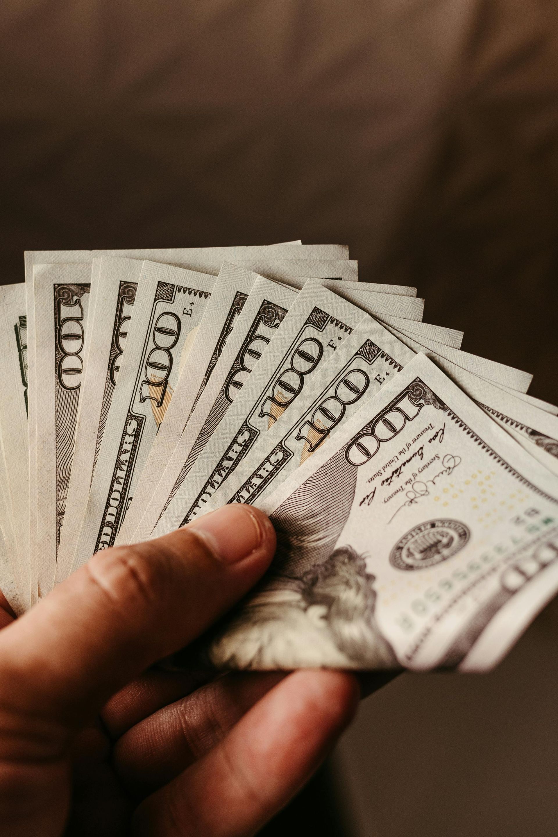 Hand holding a fan of US $100 bills against a dark background