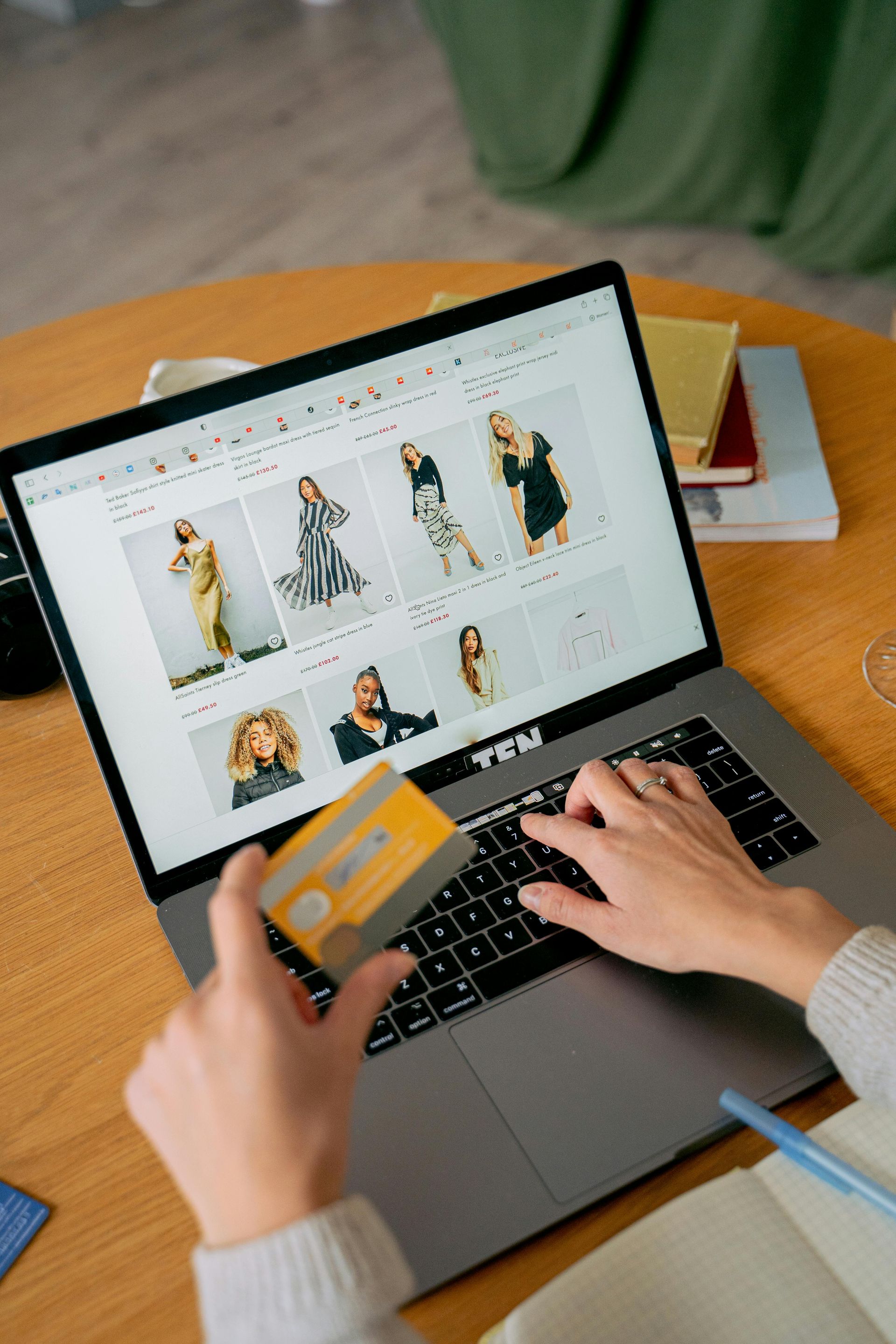 Hands using a laptop shopping website while holding a credit card at a wooden table