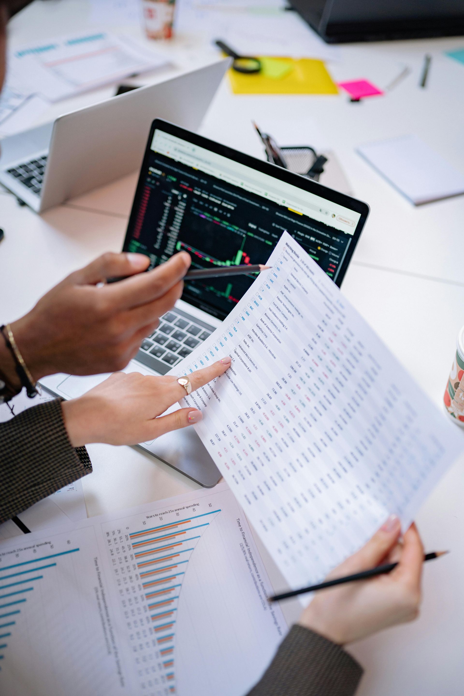 Hands reviewing printed charts beside a laptop showing analytics code on a desk