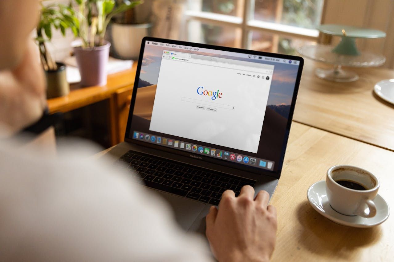 Person using a laptop with Google search open, sitting at a table with coffee.