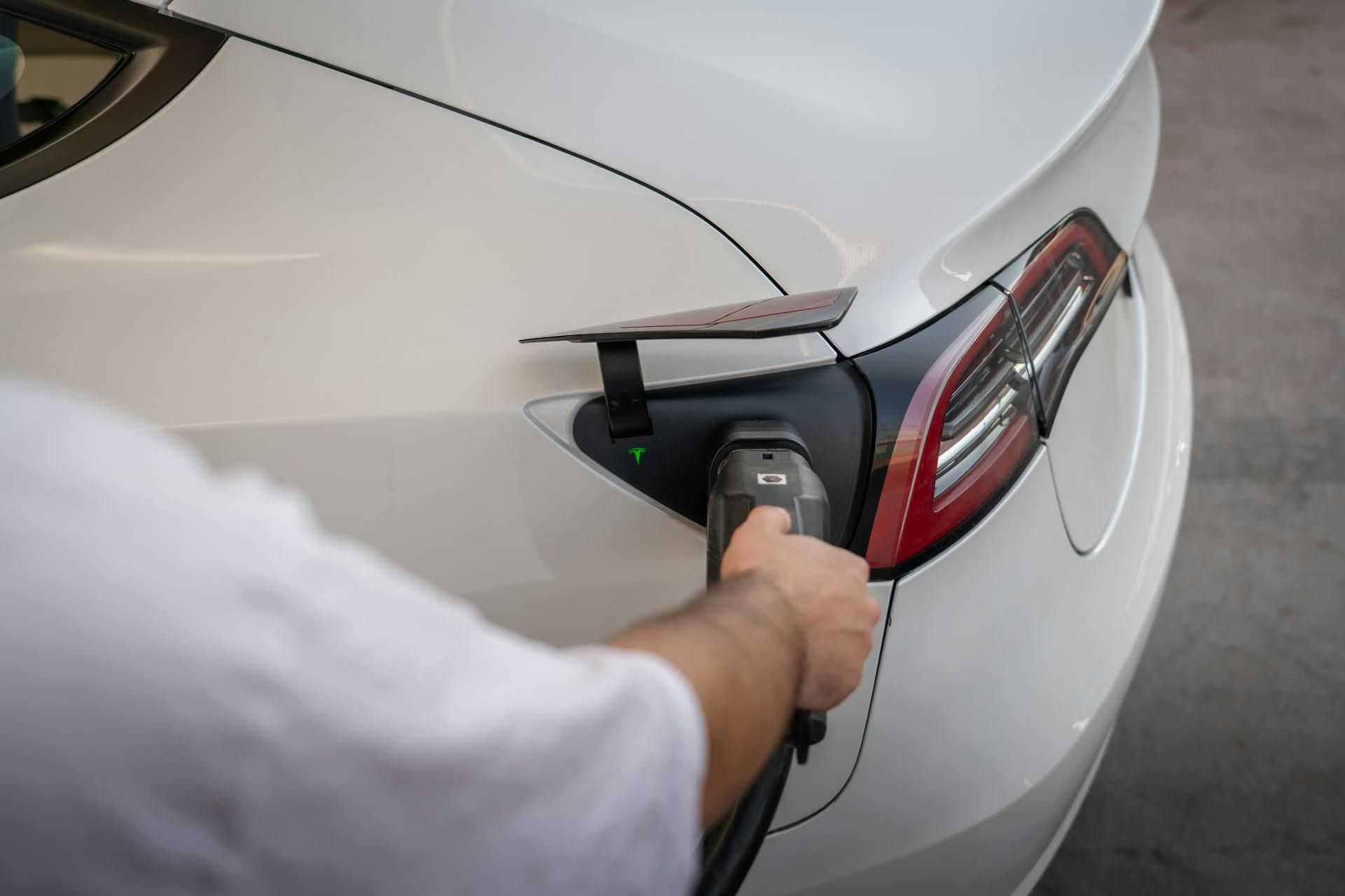 Person using a handheld buffer on a white car’s rear quarter panel and taillight area
