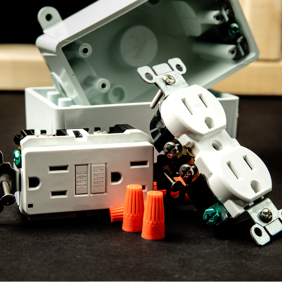 White electrical outlet with open box, plug adapter, and orange wire nuts on a black surface
