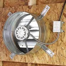 Industrial wall vent with large beige exhaust fan behind metal grille and dirty white siding.