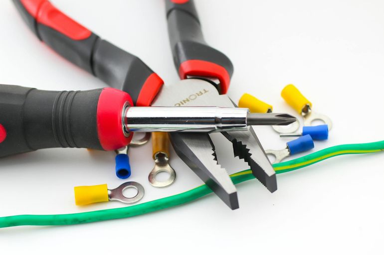 Electrical tools and wires on white background, with pliers and screwdrivers touching colored cables