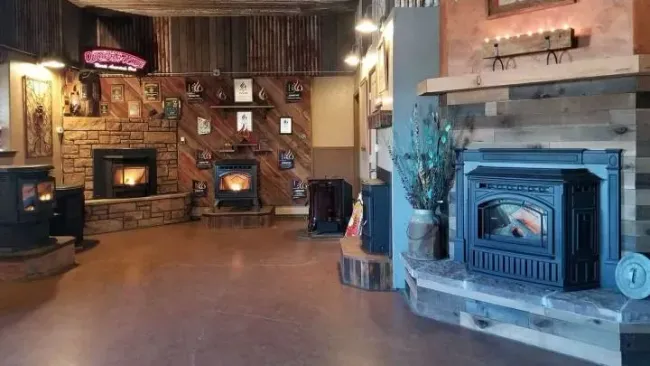 Rustic showroom with several wood stoves and fireplaces displayed in a warmly lit room