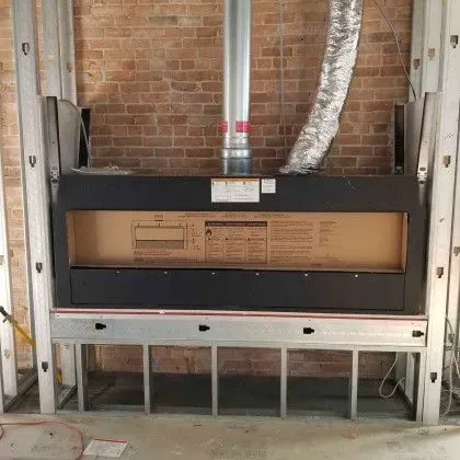 Wall-mounted HVAC unit with exposed ducting and brick wall background in a utility room