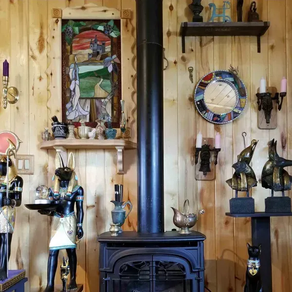 Wood-paneled room with a black stove, shelves of figurines, and a round multicolor wall clock.