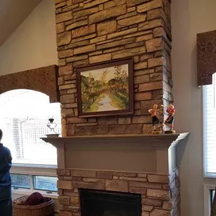 Living room fireplace with stone chimney, mantel decor, and framed landscape painting