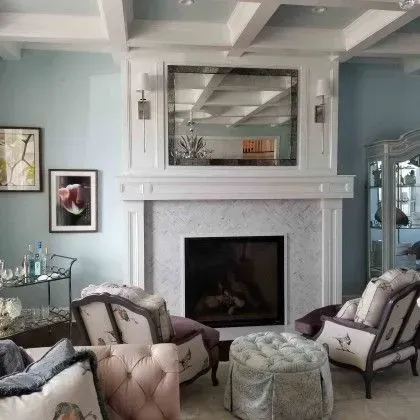 Elegant living room with a white fireplace, mirrored mantel, and tufted chairs in soft gray and lavender tones