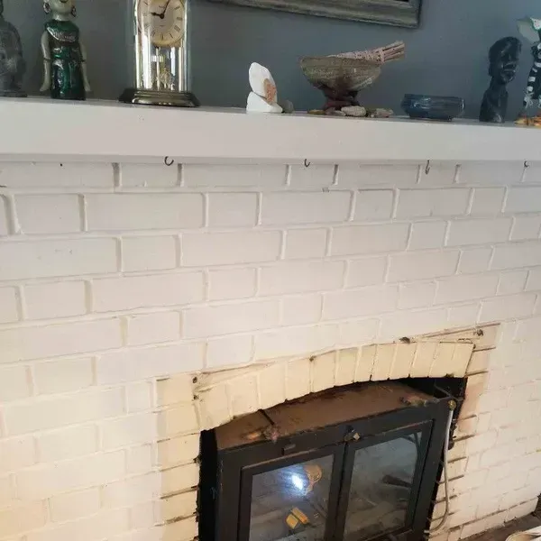 White brick fireplace with a black glass insert and mantel decor in a living room.