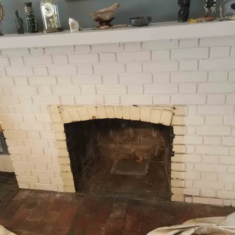 White brick fireplace with an empty firebox and red tile hearth in a room.