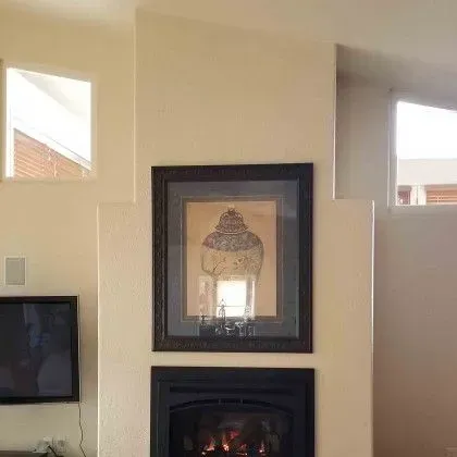 Living room wall with a framed artwork above a fireplace, flanked by two small windows and a TV on the left