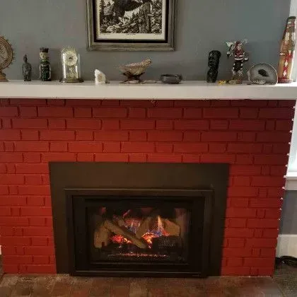 Red brick fireplace with a black firebox and mantle decor above it, with a small fire burning inside.