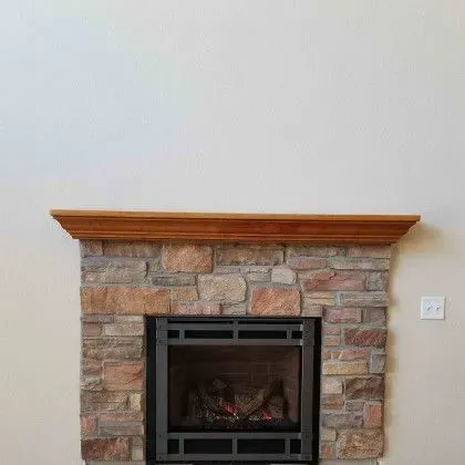 Stone fireplace with a wooden mantel against a beige wall, featuring a black metal insert.