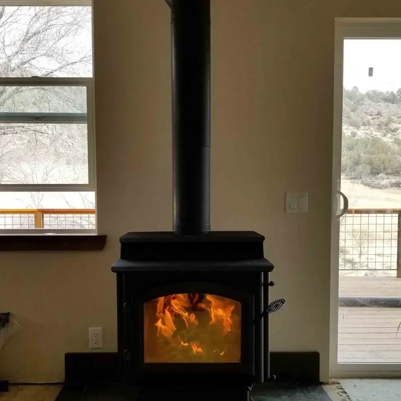 Black wood stove with a bright fire in a room, beside windows and a door to an outdoor deck