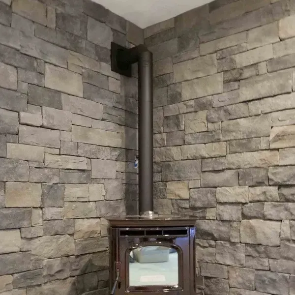 Corner stone wall with a small wood stove and black flue pipe in a room